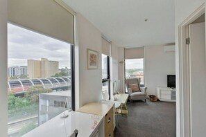 A modern hotel room with a large window, a desk, a chair, a television, and a small table. - Stylish2BD Penthouse Panoramic Views Nth Melbourne (North Melbourne)