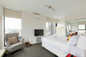 A hotel room with a bed, a television, a chair, and a large window. - Stylish2BD Penthouse Panoramic Views Nth Melbourne (North Melbourne)