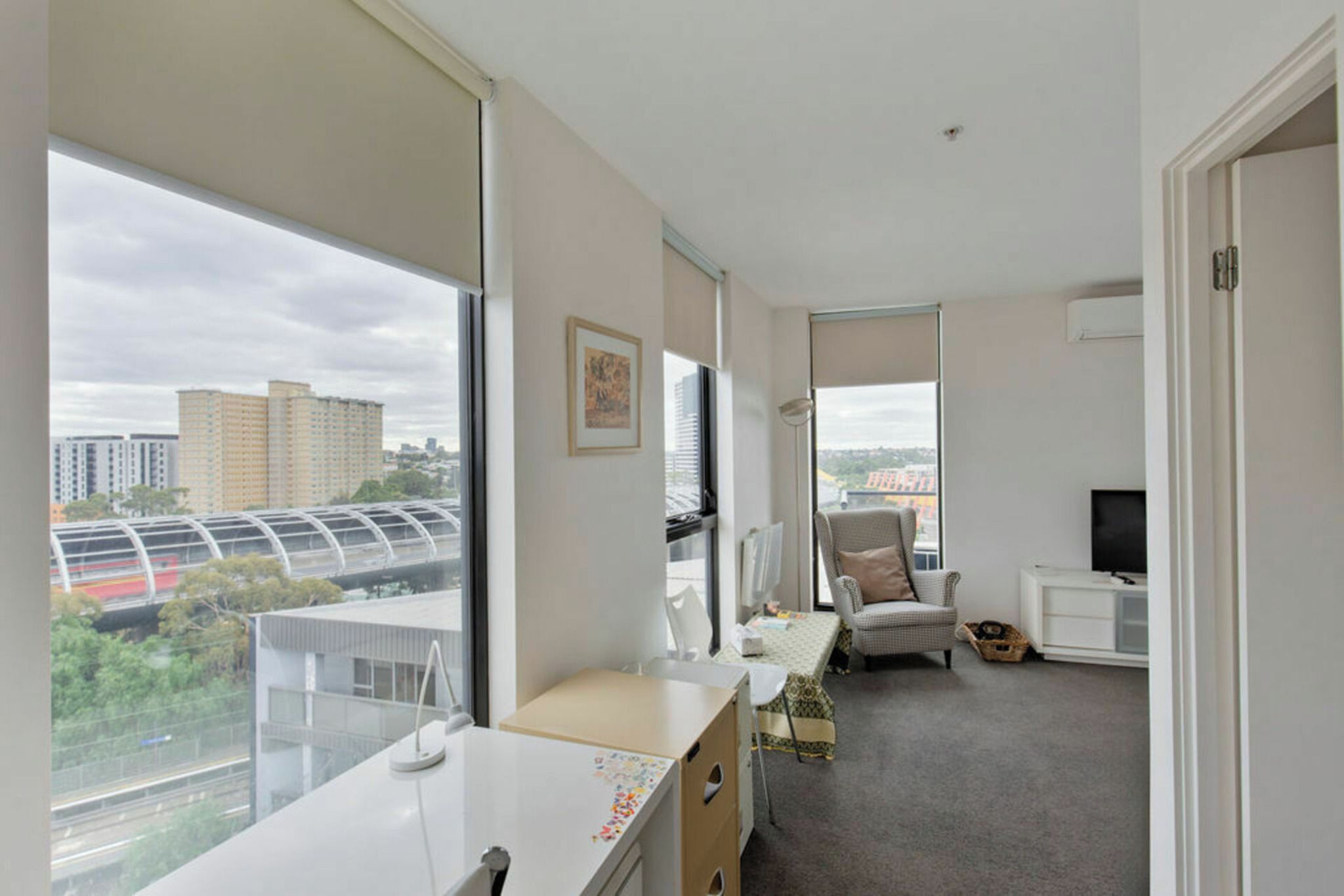 A modern hotel room with a large window, a desk, a chair, a television, and a small table.