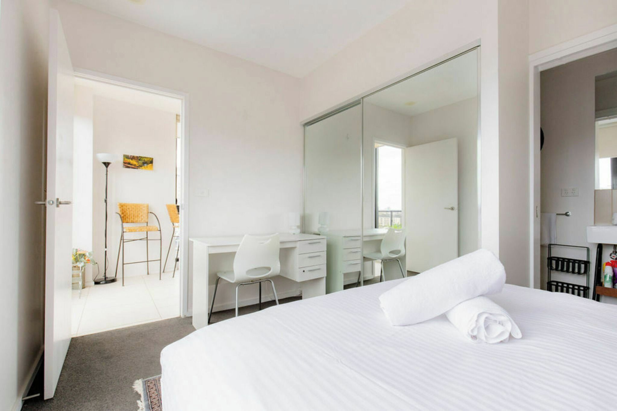 A hotel room with a large bed, a desk, a chair, a wardrobe, and a bathroom.