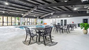 Een binnenzwembad met metalen stoelen en tafels, een betonnen vloer en een hoge plafond met zichtbare balken.