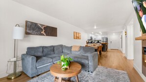 Een moderne woonkamer met een grijze bank, een ronde houten salontafel en een vloerlamp.