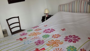 A bed with a floral-patterned bedspread, a bedside lamp, a chair, and a mirror on the wall.