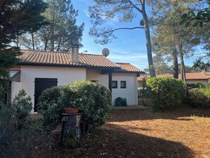 A house with a tiled roof, a satellite dish, and a small garden with a tree stump and a potted plant.