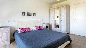 A bedroom with a bed, a wardrobe, a bedside table, and a wall-mounted light fixture.