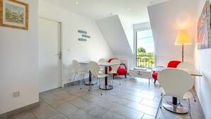 A modern dining area with a high ceiling, a dining table with chairs, a red chair, and a lamp.