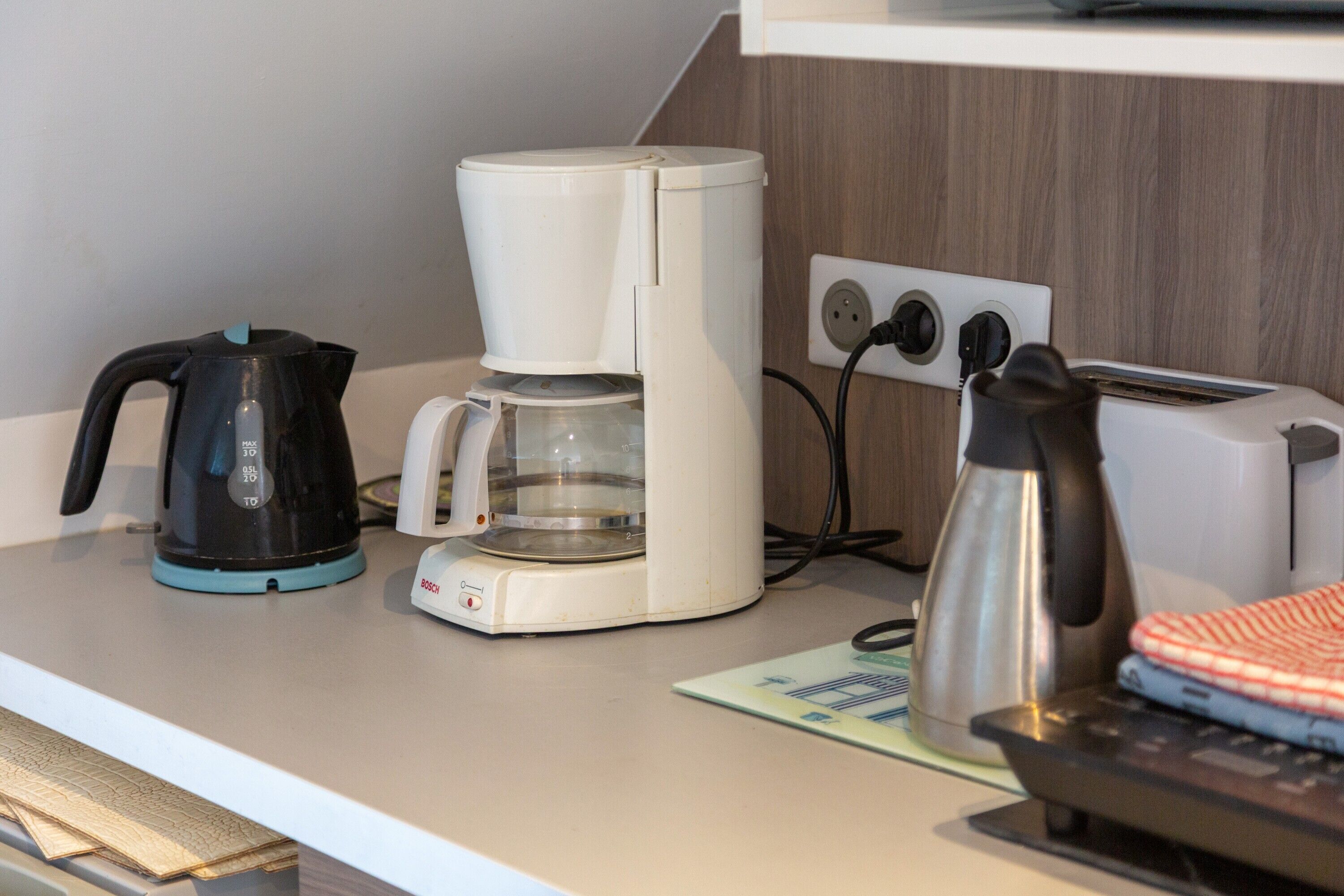 A kitchenette with a coffee maker, kettle, toaster, and a small oven on a countertop.