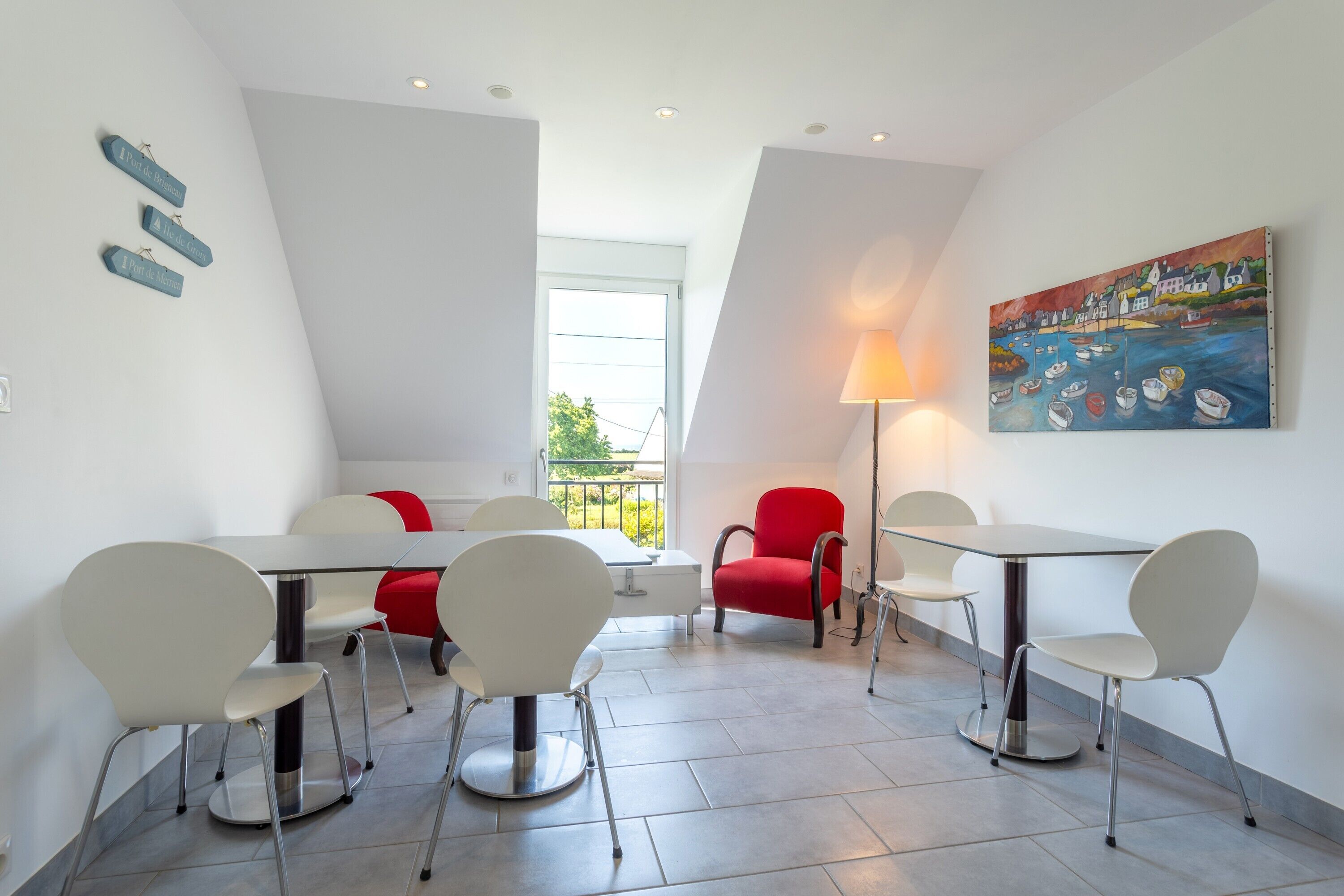 A modern dining area with white and red chairs, a table, and a painting of a harbor scene.