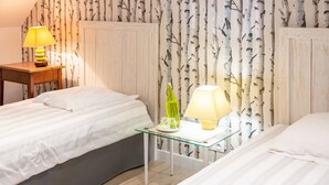 Une chambre d’hôtel avec deux lits, une table en verre avec une lampe, une bouteille et un ensemble de verres.
