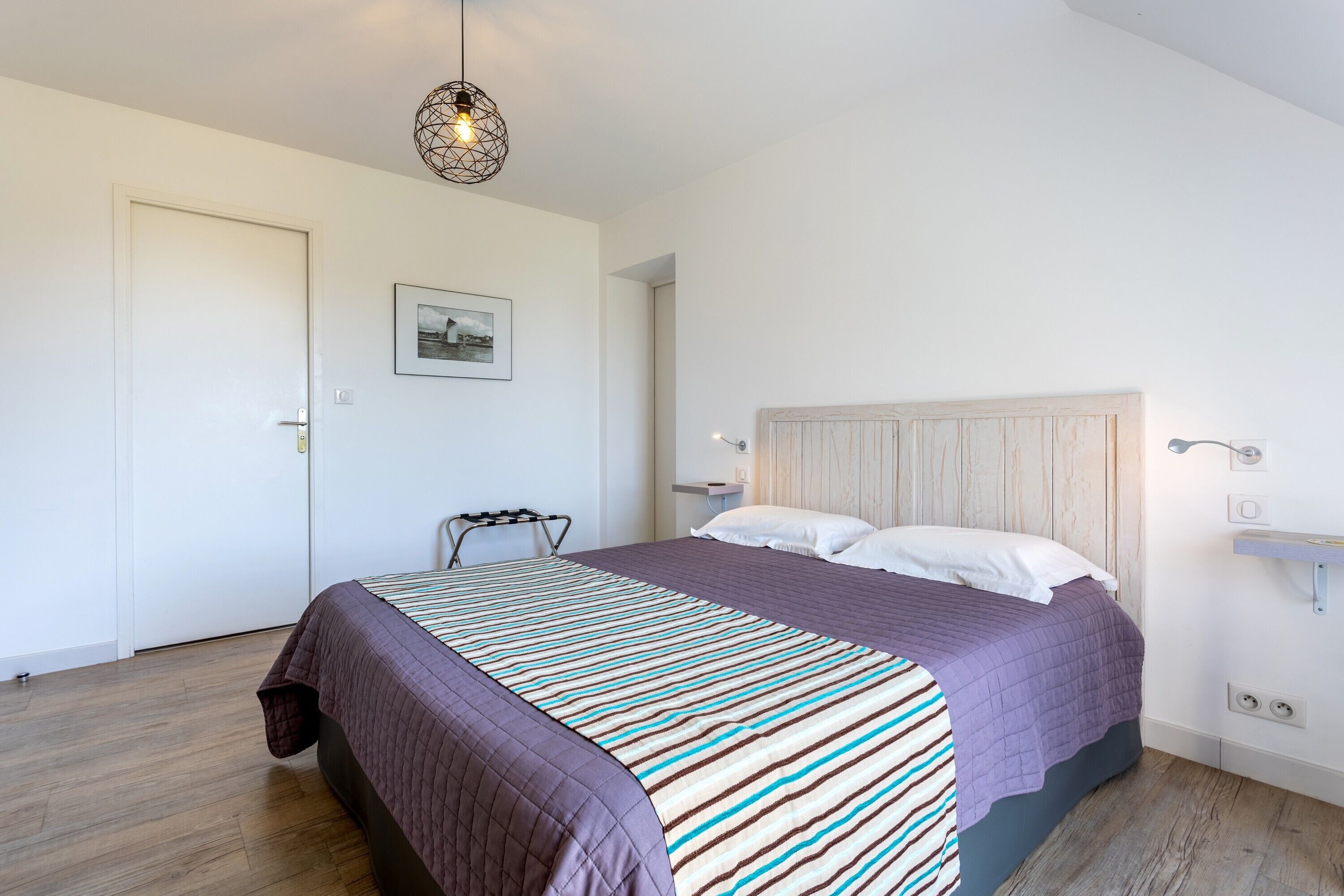 Een slaapkamer met een bed, een stoel, een hanglamp en een wandplank.