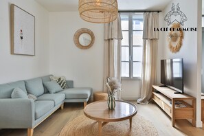 Un salon moderne avec un canapé, une table ronde en bois, un téléviseur et une grande fenêtre avec des rideaux.