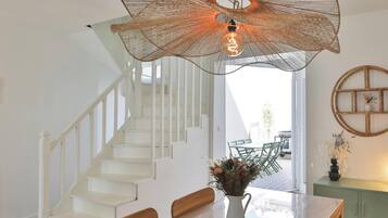 Un intérieur moderne avec un escalier, un coin repas agrémenté d’un vase de fleurs et un luminaire original en fibres tressées.