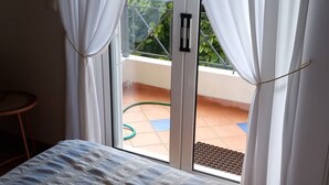 Un dormitorio con cama, cortinas blancas y una puerta corrediza de vidrio que da a un balcón.