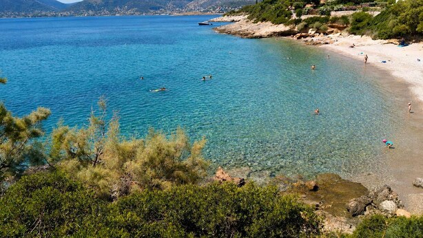 Una playa costera con agua azul cristalina, costa rocosa y vegetación.