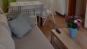 Una habitación con cama, una silla, una mesa con un control remoto, un televisor y una ventana con cortinas.