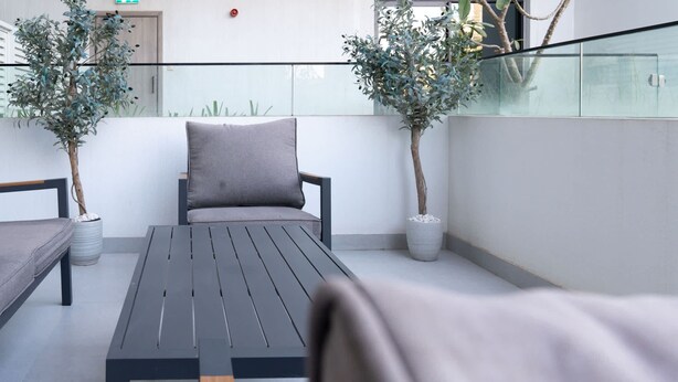 Een moderne buitenruimte met een bankje, een tafel en twee planten in potten.