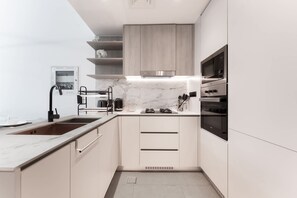A modern kitchen with a marble countertop, stainless steel appliances, and light wood cabinetry. - Free Housekeeping Visits During Your Stay - Stayshort - JVC Apartment Sleeps 2 With Huge Balcony (Dubai)
