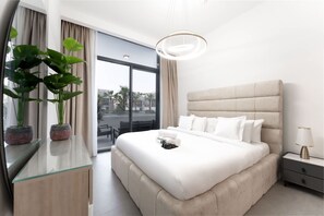 Een moderne hotelkamer met een groot bed, een glazen bureau en uitzicht op palmbomen door het raam.