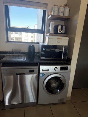 Cocina compacta con lavavajillas, lavadora Hisense, microondas y ventana con vistas a edificios.