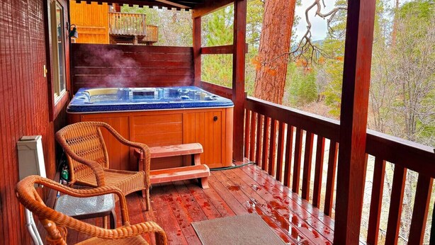 Una terraza de madera con un jacuzzi, sillas de mimbre y una cerca de madera.