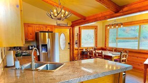Una cocina con encimera de granito, electrodomésticos de acero inoxidable, armarios de madera y un comedor con mesa y sillas de madera.