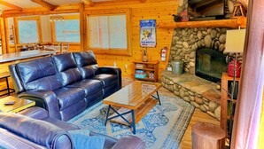 Un acogedor interior de cabaña con un sofá de cuero, una chimenea de piedra y un televisor.