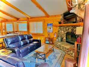 Ein gemütliches Blockhaus-Interieur mit Ledersofa, Kamin aus Naturstein und Fernseher.