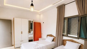 Hotellihuone, jossa on kaksi sänkyä, vaatekaappi, peili ja ikkuna, jossa on sälekaihtimet.