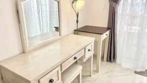 A light-colored vanity with a mirror, a bench, and a small table with drawers. - Căn Hộ View Biển (Phú Thủy)