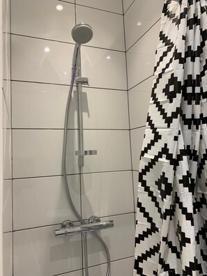 Eine Dusche mit Handbrause und ein fest installierter Armatur, ein schwarz-weiß gemustertes Duschvorhang und weiße Fliesen.