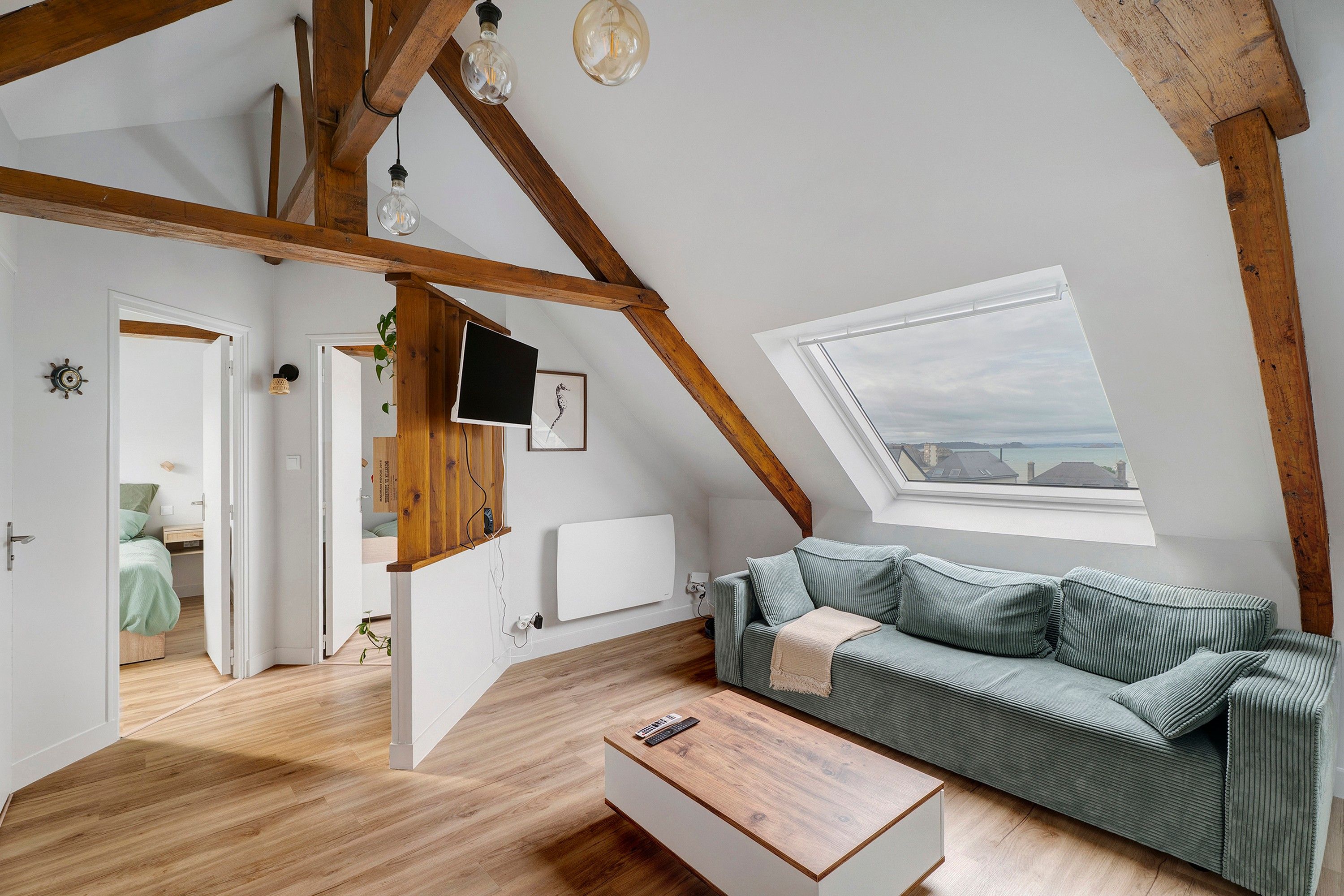 Una stanza in stile loft con soffitto spiovente, travi in legno, un divano verde, un tavolino in legno e vista tramite un lucernario.