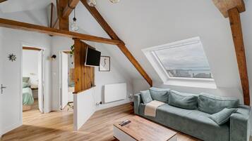 Una stanza in stile loft con soffitto spiovente, travi in legno, un divano verde, un tavolino in legno e vista tramite un lucernario.