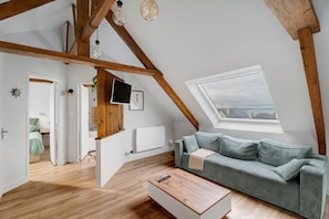 A loft-style room with a sloped ceiling, wooden beams, a green sofa, a wooden coffee table, and a view through a skylight.