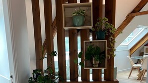 A room with a wooden slatted partition, a potted plant, a small table, and a view of the outdoors. - Apartment 'Les Fougères' with Sea View and Wi-Fi (Erquy)