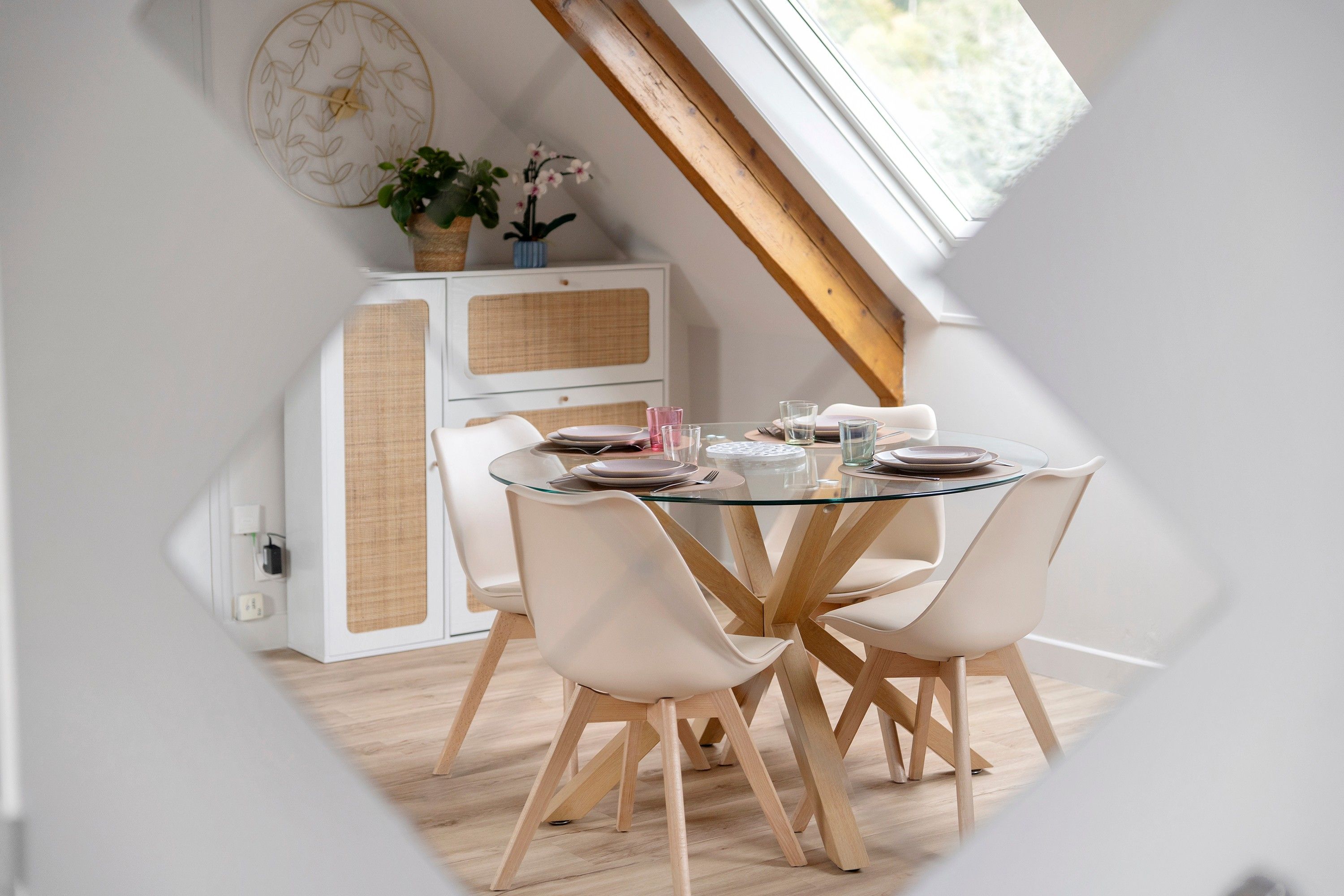 Zona pranzo con tavolo rotondo in vetro, sedie bianche e un mobile contenitore bianco con pannello intrecciato.
