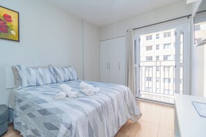 A bedroom with a bed, a desk, a wardrobe, and a window with a view of buildings. - Cozy apartment near XV de Novembro street in downtown Curitiba. (Curitiba)
