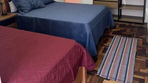 Ein Schlafzimmer mit zwei Betten, einem Kleiderschrank und einem Parkettboden mit Fischgrätmuster.