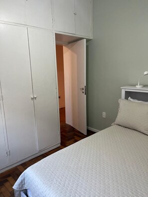 Une chambre à coucher comprenant un lit, une table de chevet, une armoire et une porte ouverte donnant sur une autre pièce.
