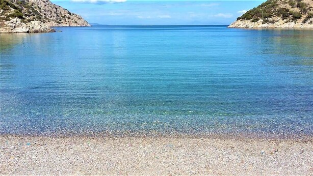 Una masa de agua tranquila con una orilla pedregosa y colinas rocosas al fondo.