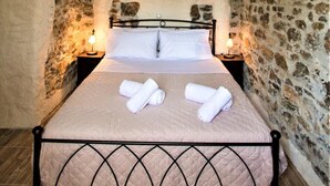 Un dormitorio con ventilador de techo de madera, paredes de piedra, cama con colcha y dos lámparas de noche.
