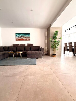 A modern living room with a sectional sofa, a coffee table, a potted plant, and a dining area with chairs.