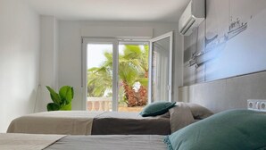 Un dormitorio con cama, una planta en maceta y vistas a palmeras a través de una puerta abierta.