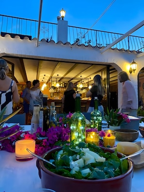 Un área de comedor al aire libre con mesas dispuestas para comidas, rodeada de plantas en macetas y velas.