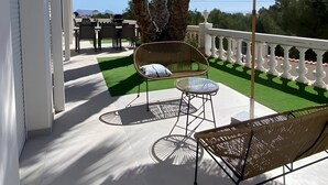Un balcón con un toldo de paja, una silla de mimbre, una mesa de vidrio y un sofá.