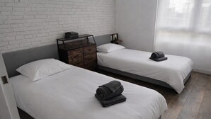 Quarto de hotel com duas camas, cômoda de madeira e parede de tijolos.