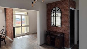 Um quarto com parede de tijolos, uma grande janela em arco, um banco de madeira e um candelabro com várias lâmpadas.