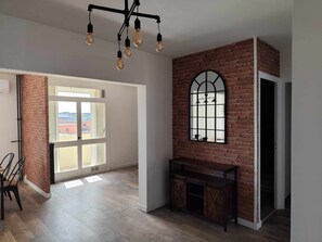 Ein Zimmer mit einer Ziegelwand, einem großen Bogenfenster, einer hölzernen Bank und einer Chandelieber mit mehreren Leuchten.