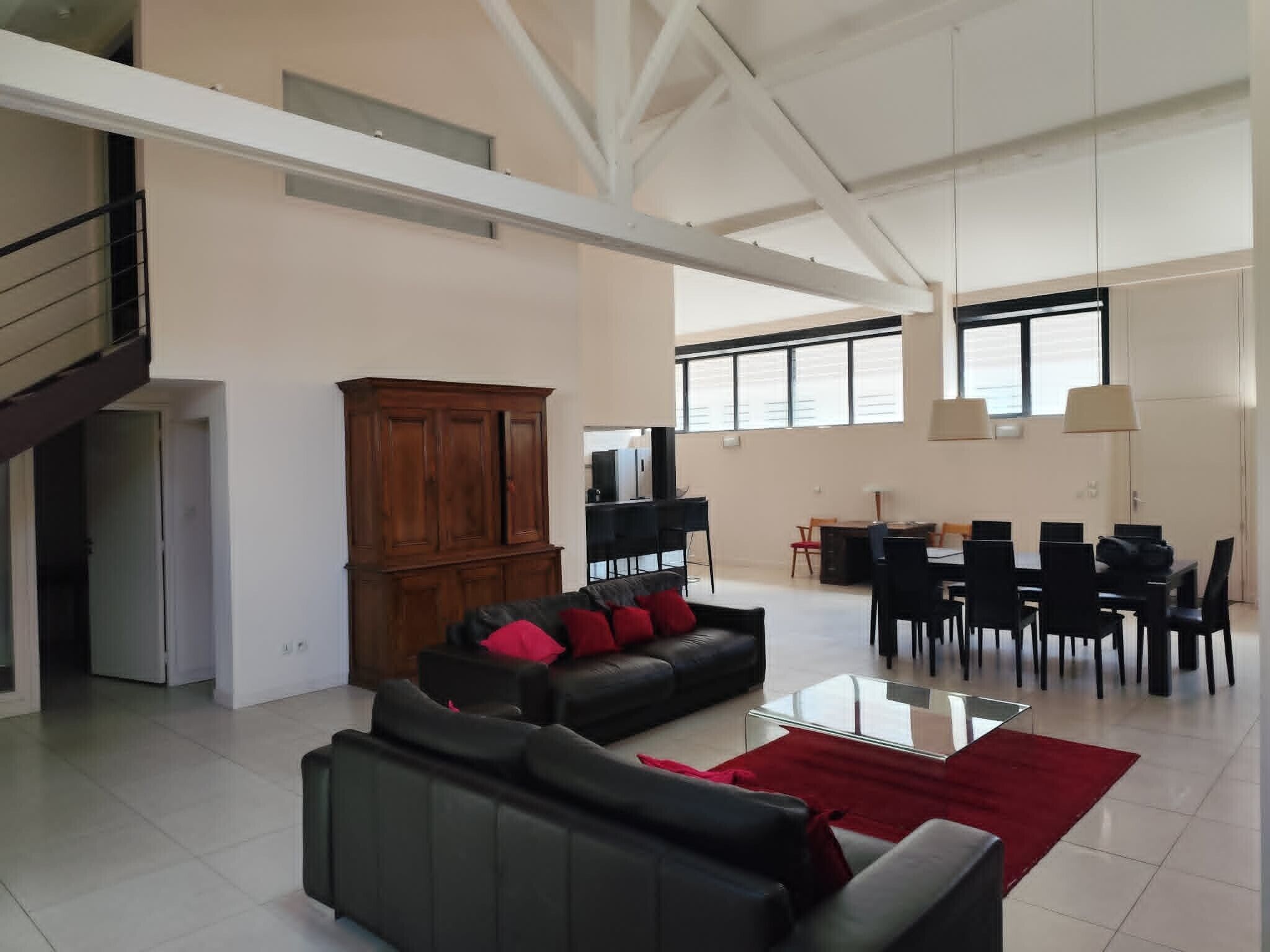 Un salon spacieux avec un canapé en cuir noir, un meuble en bois et un coin repas comprenant des chaises et une table, le tout dans des tons noirs.