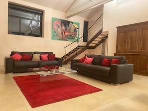Un salon avec deux canapés, une table basse, un tapis rouge, un escalier et un meuble en bois.