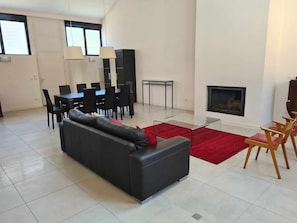 Un salon moderne avec un canapé noir, une table à manger, des chaises et une cheminée.